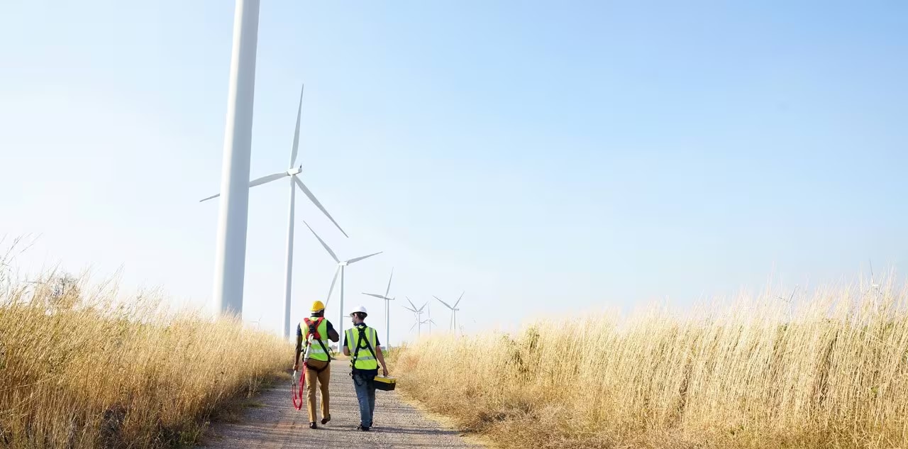 Technicians walking near a windmill in a field