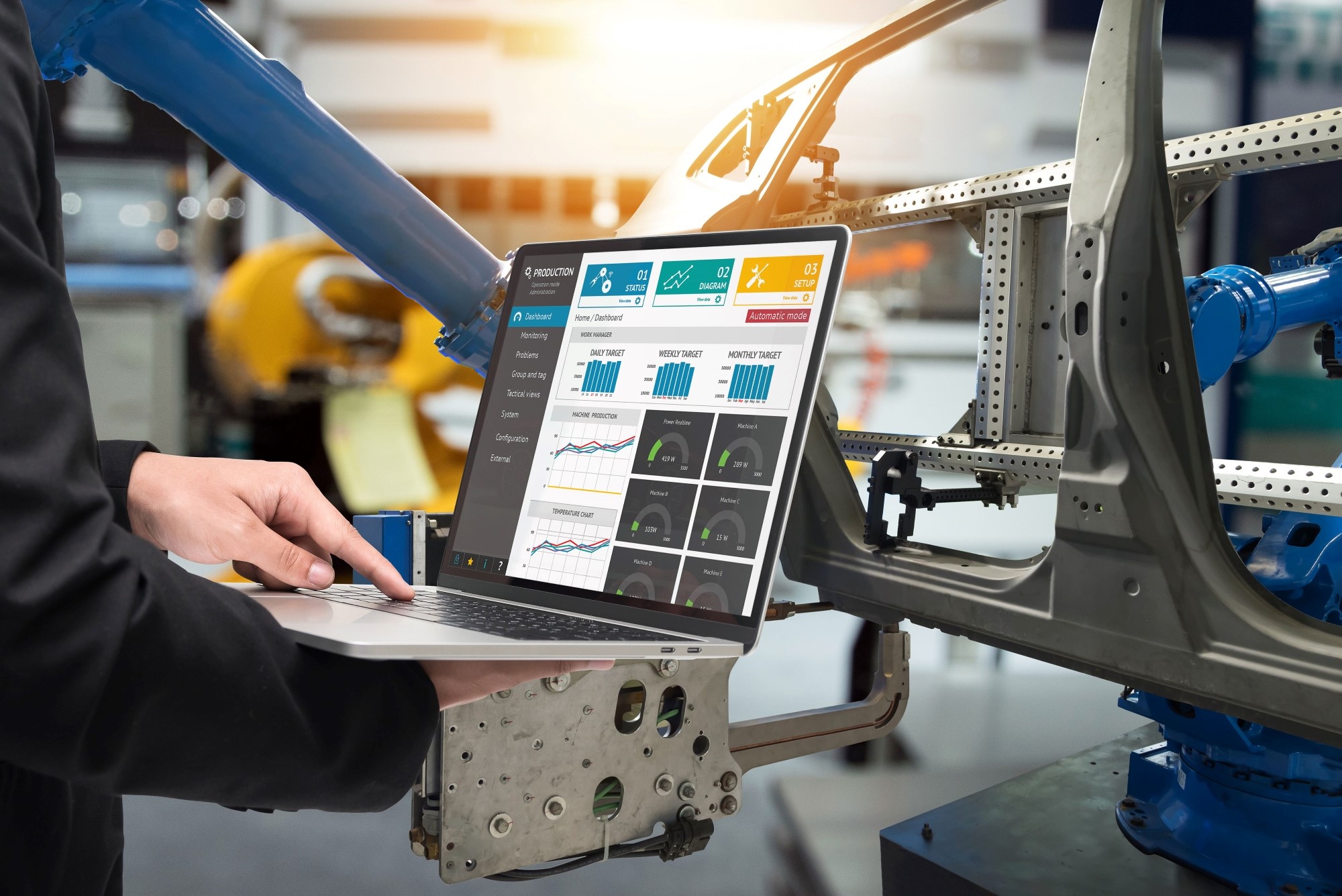 手持显示数据分析与图表的笔记本电脑，站在工业场景中正在汽车框架上作业的机械臂旁。