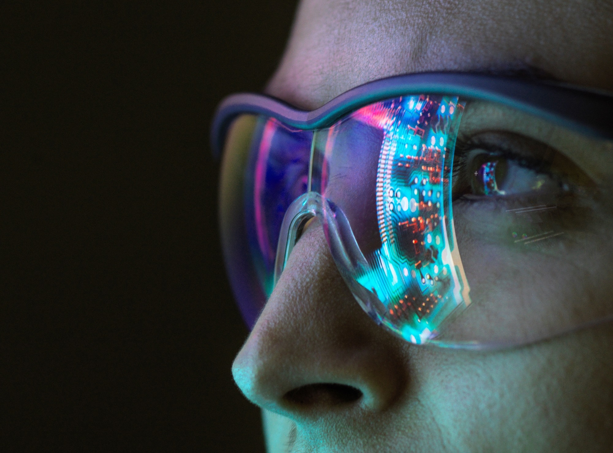 A person wearing glasses with a clear reflection of a circuit board visible on the lenses.