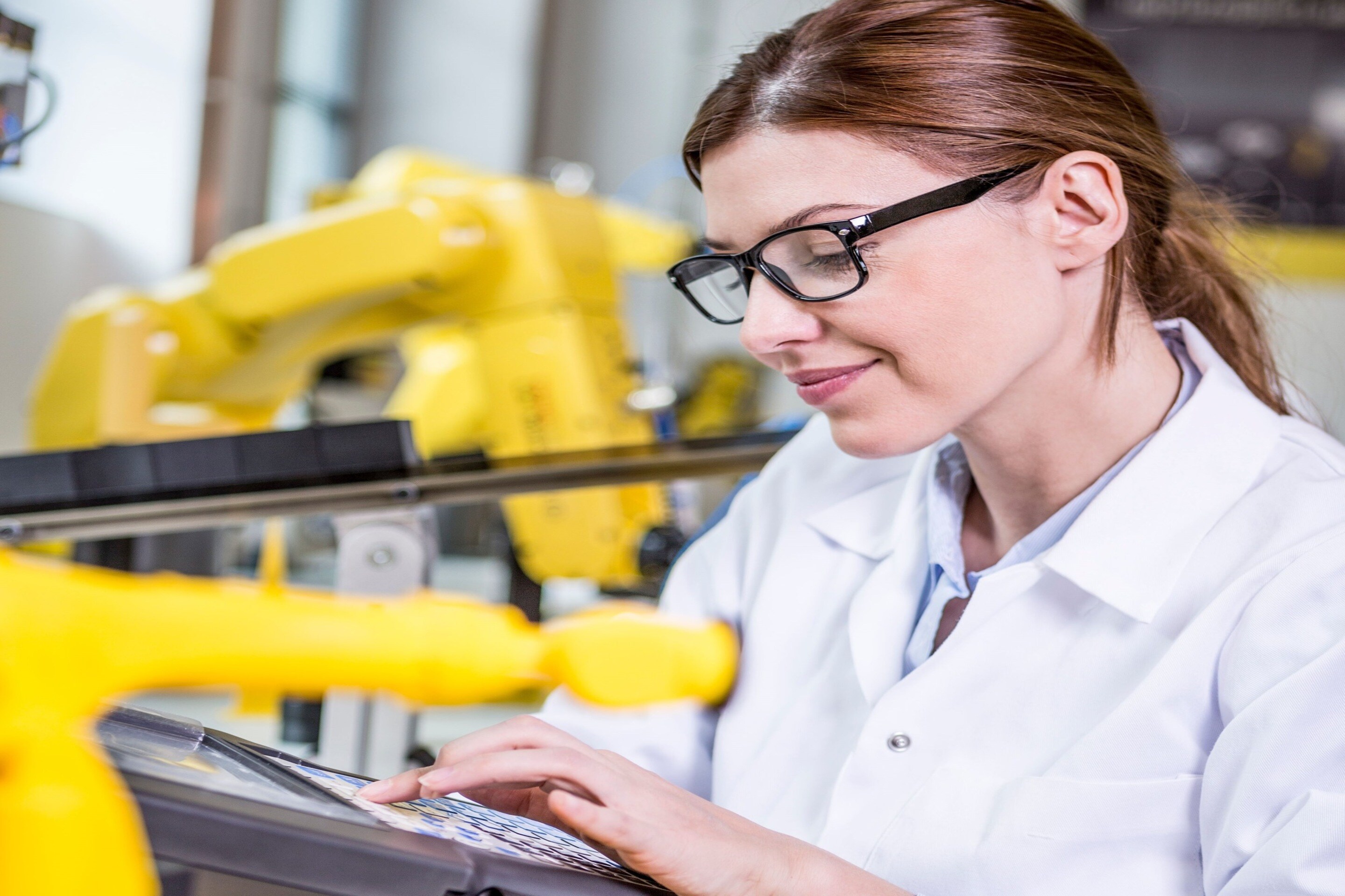 Woman using device in factory with industrial robots.