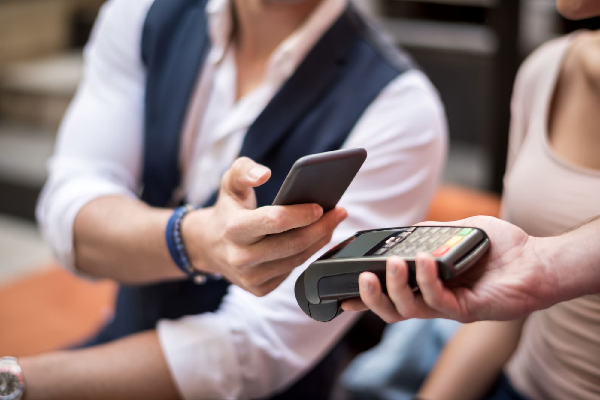 一个人手持智能手机靠近支付终端并进行非接触式支付，而另一个人则手持该终端。