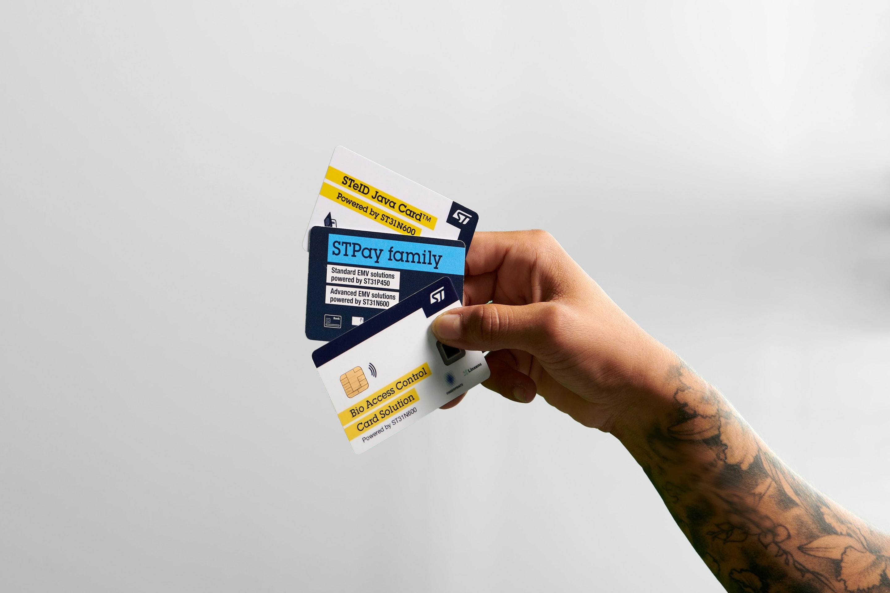 手持三张卡：“生物门禁卡解决方案”、“STPay系列”卡和“STID即触即用”卡，均带有意法半导体标识。