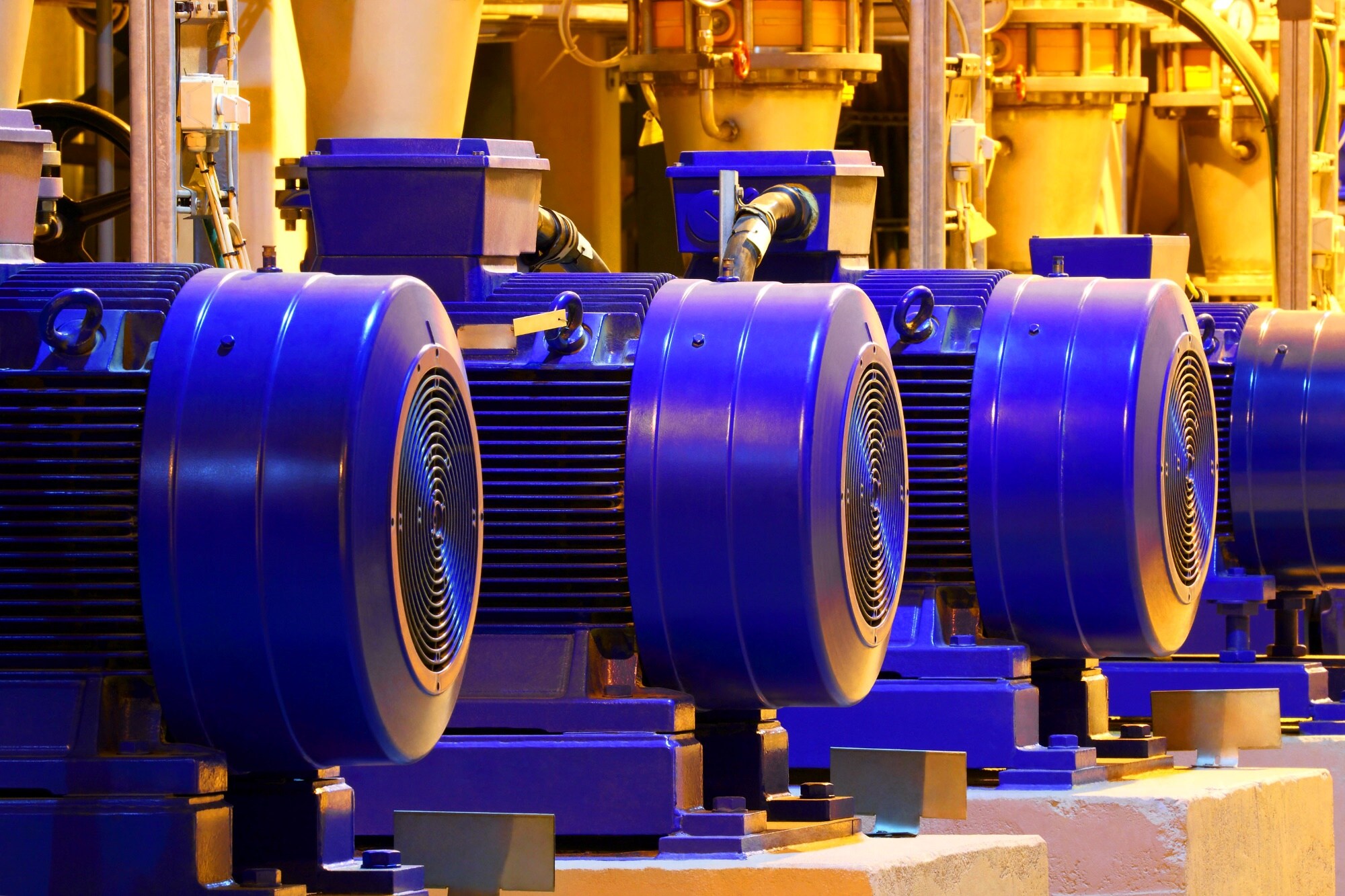 工厂内安装的大型蓝色工业电机，背景是黄色管道和设备。
